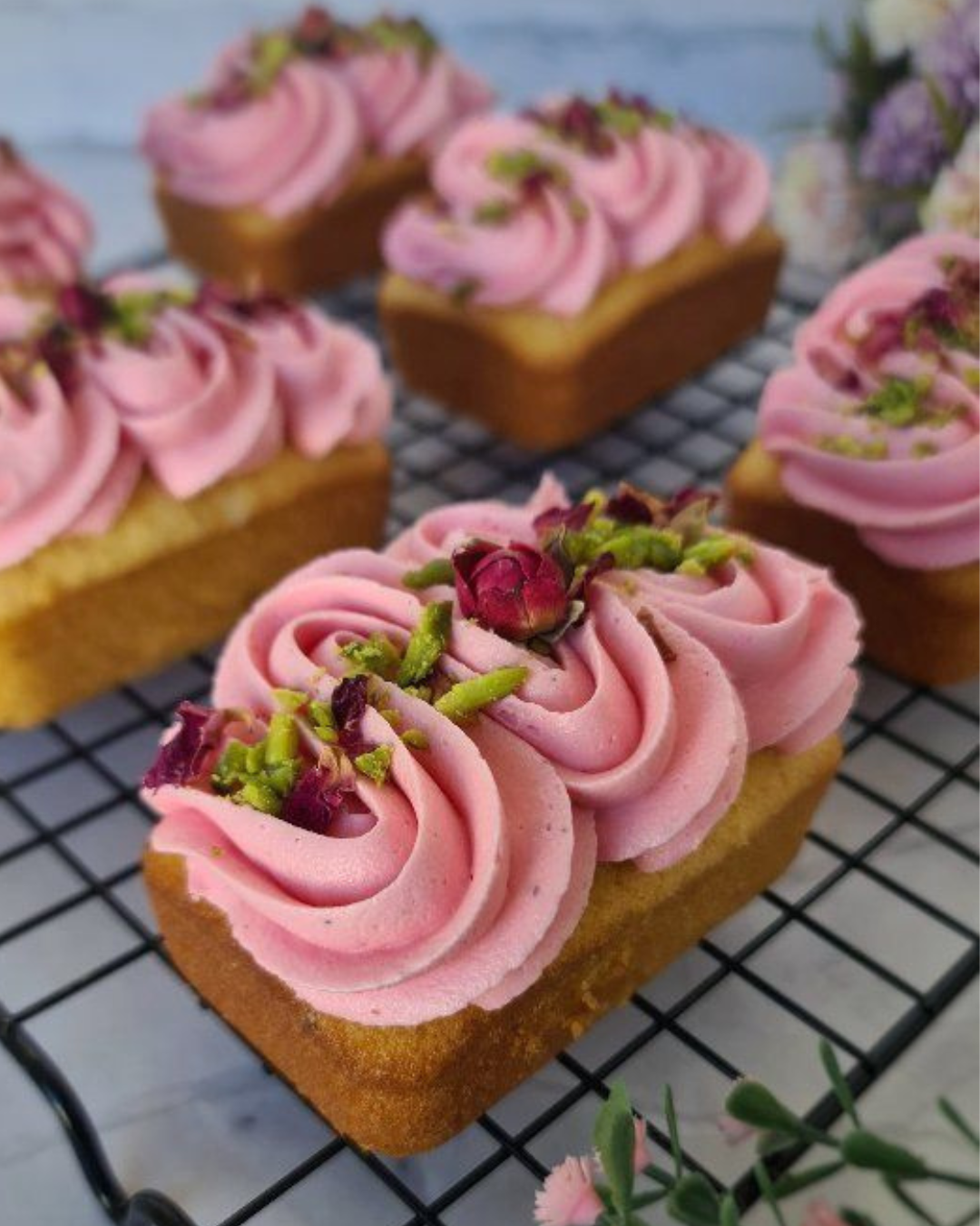 Financiers met roze frosting en rozentopping op een bakrooster.